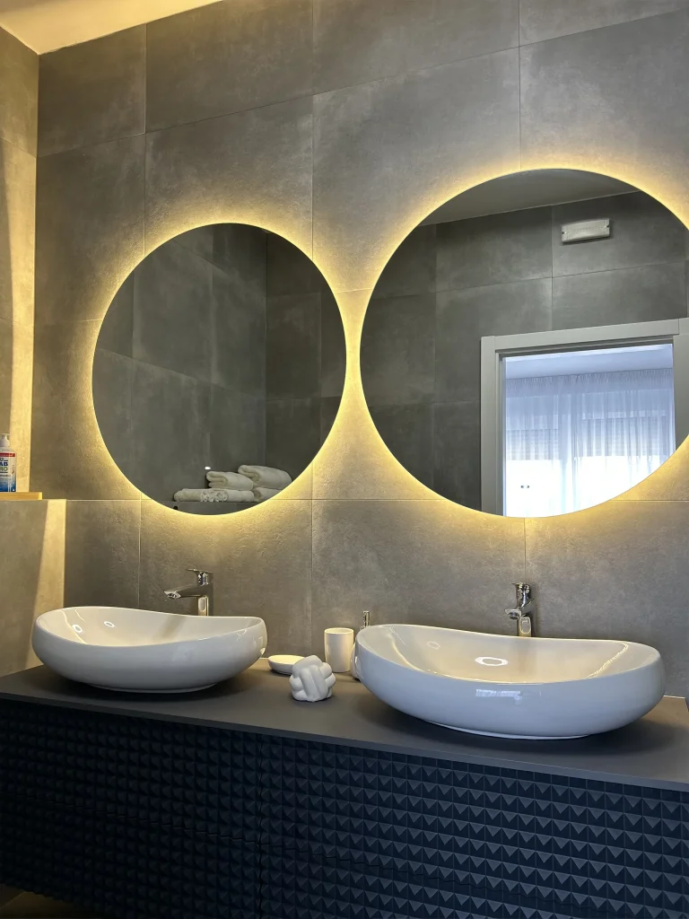 Modern bathroom with two round backlit mirrors and stylish double sinks – Moderna kupaonica s dva okrugla ogledala s pozadinskim osvjetljenjem i elegantnim dvostrukim umivaonicima.