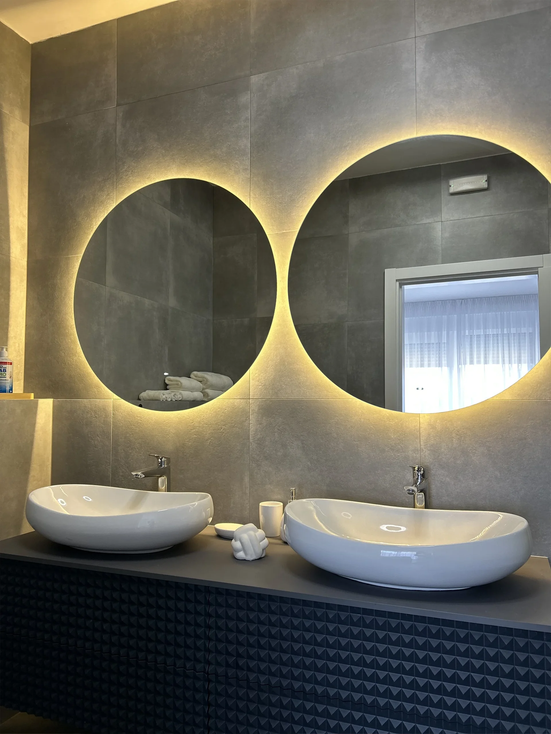 Modern bathroom with two round backlit mirrors and stylish double sinks – Moderna kupaonica s dva okrugla ogledala s pozadinskim osvjetljenjem i elegantnim dvostrukim umivaonicima.